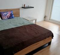 Pekný 1 izbový byt, Tilgnerova ulica, Bratislava IV. Karlova Ves - Spálňa v 1-izbovom byte s posteľou, kreslom a podlahou s dreveným dekorom.