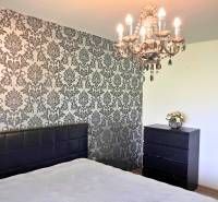 Rodinný dom v obci Dubová s 920m2 rozsiahlym pozemkom  - Spálňa s lustrom a tapetovou stenou v rodinnom dome. Podlaha s dreveným dekorom.