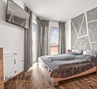 NA PREDAJ 2-IZBOVÝ BYT S 2 BALKÓNMI, DUNAJSKÁ STREDA - Spálňa v 2-izbovom byte s televízorom, posteľou a podlahou s dreveným dekorom.