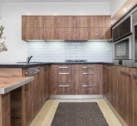 PREDAJ-2 IZBOVÝ BYT-KOMPLETNÁ REKONŠTRUKCIA - RUŽINOV - Kuchyňa v 2-izbovom byte s drevenými skrinkami, bielym obkladom a podlahou s dreveným dekorom.