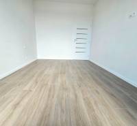 3i. BYT S VLASTNÝM TEP. ČERPADLOM + KLIMATIZÁCIA A EXTERIÉROVÉ ŽALÚZIE - Izba v 3-izbovom byte s drevenou podlahou a bielymi stenami.