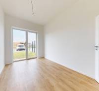 3i. BYT SO ZÁHRADOU +TEP. ČERPADLO, KLIMATIZÁCIA A ŽALÚZIE V CENE - Priestranná miestnosť s bielymi stenami a drevenou podlahou v 3-izbovom byte.