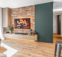 PRENÁJOM 3 izbový byt s predzáhradkou, BORY PROMENÁDA - Obývačka v 3-izbovom byte s tehlovou stenou, krbom a podlahou s dreveným dekorom.