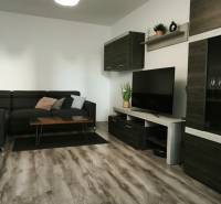 Prenajmeme 3 izb  byt na Korytnickej ulici - Obývačka v 3-izbovom byte s tmavou sedačkou a podlahou s dreveným dekorom.