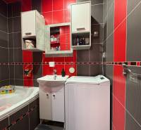 Na predaj: Investičný 3 izb.byt + murovaná PIVNICA - Kúpeľňa v 3-izbovom byte so sprchovacím kútom a práčkou, červené a sivé obklady.
