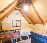 PREDANÉ CHATA NA PREDAJ PÁR METROV OD BUKOVSKEJ PRIEHRADY - Podkrovná izba v chate so strešnými trámami a jednoduchým nábytkom.