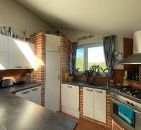 PREDAJ krásny 6 izb. rod. dom prepojený s prírodou - Kuchyňa v rodinnom dome má tehlový obklad, biele skrinky a plynový sporák.