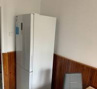 Priestranný 2-izbový byt (62 m²) s Lodžiou, Nobelova – Nové Mesto - Kuchyňa v 2-izbovom byte s bielou chladničkou a drevenými obkladmi na stenách.