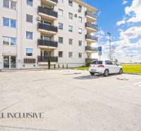 NA PRENÁJOM 2x 2-IZBOVÉ BYTY S TERASOU,DUNAJSKÁ STREDA - Parkovisko pred bytovým domom na Panónskom háji v Dunajskej Strede, s autami a trávnatou plochou.