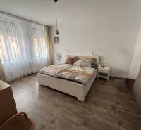 Veľký 96 m2  2 izbový byt s garážovým státím Topoľčany Centrum  - Spálňa v 2-izbovom byte s veľkými oknami, posteľou a podlahou s dreveným dekorom.