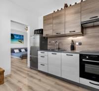 REZERVOVANÉ Predaj moderný 1-izbový byt, 45,24m2, Bratislava IV - Kuchyňa v 1-izbovom byte s chladničkou, dekorom dreva a obrazom pláže v pozadí.