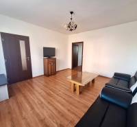 REZERVOVANÝ 2,5 IZBOVÝ BYT, 65 M2,PREŠOV,UL. FEDERÁTOV - Obývačka v 3-izbovom byte s podlahou s dreveným dekorom, čiernou sedačkou a televízorom.