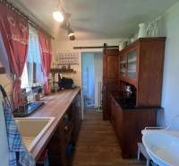 !! NOVÁ CENA !! predaj romantickej chalúpky v Šípkove  - Kuchyňa v drevenej chate s rustikálnym nábytkom, umývadlom a dekoratívnymi záclonami.