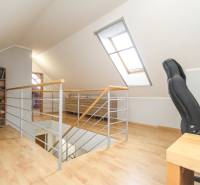 4i mezonet, 133m2, vlastné kúrenie, Melčice-Lieskové - Podkrovná časť 4-izbového bytu s pracovnou stoličkou a knihovničkou, podlaha s dreveným dekorom.