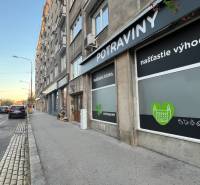 BA/STARÉ MESTO - Prenájom kompletne zariadeného 2i bytu s 2 balkónmi - Ulica Krížna v Bratislave, vedľa cesty sa nachádzajú potraviny s reklamnými nápismi.