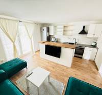 Novostavba 3i bytu s parkovaním, Dvorníky - Obývacia izba s kuchyňou v 3-izbovom byte, podlaha s dreveným dekorom, elegantné závesy.