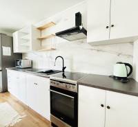 Novostavba 3i bytu s parkovaním, Dvorníky - Kuchynská linka v 3-izbovom byte s bielymi skrinkami a podlahou s dreveným dekorom.