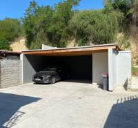 Novostavba 3i bytu s parkovaním, Dvorníky - Prístrešok pre auto v Dvorníkoch s betónovým povrchom a prírodným pozadím.