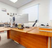 Obchodné, administratívne, priestory, showroom v exponovanej časti TT - Kancelárske priestory s dreveným stolom, počítačom a dekoračnými predmetmi na stenách.