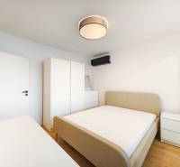 Prenájom úplne nového 2 izb. bytu - skvelá poloha a komfortné bývanie. - Spálňa v 2-izbovom byte s posteľou, skriňou, komodou a podlahou s dreveným dekorom.