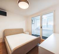 Prenájom úplne nového 2 izb. bytu - skvelá poloha a komfortné bývanie. - Spálňa v 2-izbovom byte s posteľou, stolíkom a balkónom, podlaha s dreveným dekorom.