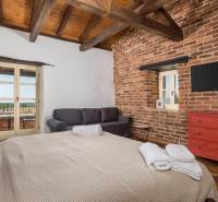 Na predaj KAMENNÝ DOM s LUXUSOM v srdci Istrie - Spálňa vo vile s tehlovými stenami, TV, pohovkou a veľkou posteľou.