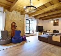 LUKRATÍVNA CHATA - NOVOSTAVBA - SRDCE VRÁTNEJ DOLINY - Interiér Chaty s kamennou stenou, veľkým gaučom a podlahou s dreveným dekorom.