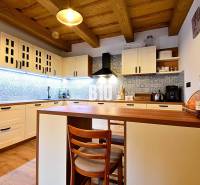 LUKRATÍVNA CHATA - NOVOSTAVBA - SRDCE VRÁTNEJ DOLINY - Kuchyňa v chate s dreveným stropom, podlahou s dreveným dekorom a modrými obkladmi.