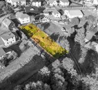 Stavebný pozemok - Turzovka - stavebné povolenie - Pozemok na bývanie v Turzovke, obklopený domami, s trávnatým porastom a stromami.