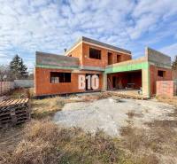 6 izbový rodinný dom  - DVOJGARÁŽ - CABAJ časť Riegler - Nedokončená stavba tehlového rodinného domu, obklopená trávou a drevenými paletami.