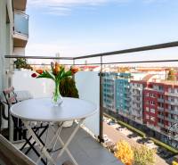 TOP lokalita na začiatku Petržalky, DVE VEŽE, Bosákova ul. - Balkón na Bosákovej ulici, Bratislava - Petržalka s výhľadom na budovy, stôl s kvetinami.