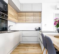 TOP lokalita na začiatku Petržalky, DVE VEŽE, Bosákova ul. - Kuchyňa v 2-izbovom byte s lakovanými skrinkami, podlahou s dreveným dekorom a vázou kvetov.