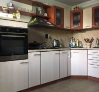 Dom s garážou na peknom rovinatom pozemku so šírkou 24m. - Kuchyňa v rodinnom dome s podlahou s dreveným dekorom a svetlými skrinkami.