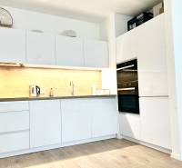 PRENÁJOM exkluzívny 2 izb byt POPRAD s loggiou 53,9 + 8,34 m2 - Kuchyňa v 2-izbovom byte s bielymi skrinkami a podlahou s dreveným dekorom.