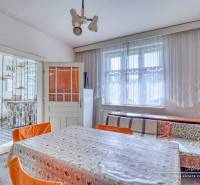 REZERVOVANÉ Starší 2-izbový rodinný dom v obci Dobrá Voda - Jedáleň v rodinnom dome s veľkým oknom, kvetinovým obrusom a oranžovými stoličkami.