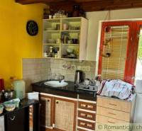 Záhrada s chatkou pod Malými Karpatami, Sološnica - Kuchyňa v chate s dreveným stropom a žltou stenou, vybavená základným riadom.