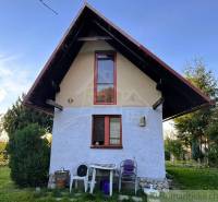 Záhrada s chatkou pod Malými Karpatami, Sološnica - Chata v Sološnici so strmou strechou, okná, príroda a plastové stoličky.