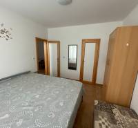 Predaj budovy v centre mesta - Spálňa s posteľou, skriňou a zrkadlom v rodinnom dome s podlahou s dreveným dekorom.