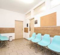 Na predaj ambulancia 101m2, Bratislavská ul. - Žilina - Čakáreň s modrými stoličkami, korkovou nástenkou a podlahou s dreveným dekorom v kancelárii.