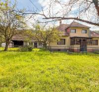 5i RD s garážou, Čierna Lehota, okr. Bánovce n./B. - Rodinný dom v Čiernej Lehote s trávnikom, stromami a oplotením na pozemku.