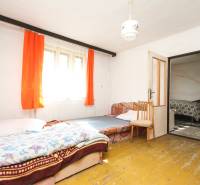 5i RD s garážou, Čierna Lehota, okr. Bánovce n./B. - Izba s posteľou a kreslom, podlaha s dreveným dekorom, oranžové závesy, rodinný dom.