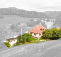 5i RD s garážou, Čierna Lehota, okr. Bánovce n./B. - Rodinný dom v Čiernej Lehote obklopený zeleňou, mierne kopcovitá krajina v pozadí.