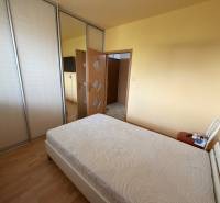 3 izbový byt  balkónom Topoľčany Juh - Spálňa v 3-izbovom byte s posteľou, šatníkovými skriňami a podlahou s dreveným dekorom.