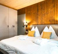 Na predaj krásny apartmám v Štrbe - Spálňa v 2-izbovom byte s posteľou, skriňou a stenou s dreveným dekorom.