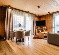 Na predaj krásny apartmám v Štrbe - Obývačka v 2-izbovom byte s podlahou s dreveným dekorom, sedačkou a jedálenským stolom.