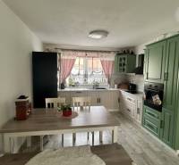 REZERVOVANÉ - Predaj, rodinný dom Malinová - NOVOSTA... - Kuchyňa v rodinnom dome so zelenou linkou, jedálenským stolom a červenými závesmi.