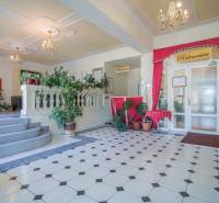 Predaj nehnuteľnosti v mestskej časti Poprad-Veľká - Hotelová recepcia s rastlinami a lustrami, dlažba s geometrickým vzorom.