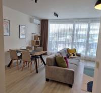 PRENÁJOM - 3 izbový byt Nitra – RIVIERA NITRA, Piesková ulica - Obývacia izba v 3-izbovom byte obsahuje sedačku, jedálenský stôl a veľké okno.