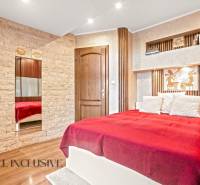 NA PREDAJ 5+2 IZBOVÝ RD PRI KÚPALISKU, DUNAJSKÁ STREDA - Spálňa v rodinnom dome s postelí, kamennými detailmi a podlahou s dreveným dekorom.