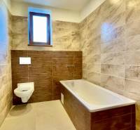 Predaj novostavba rodinného domu   Nová Baňa - Kúpeľňa s obkladmi v dekore dreva a dlažbou, vaňa a závesná toaleta.